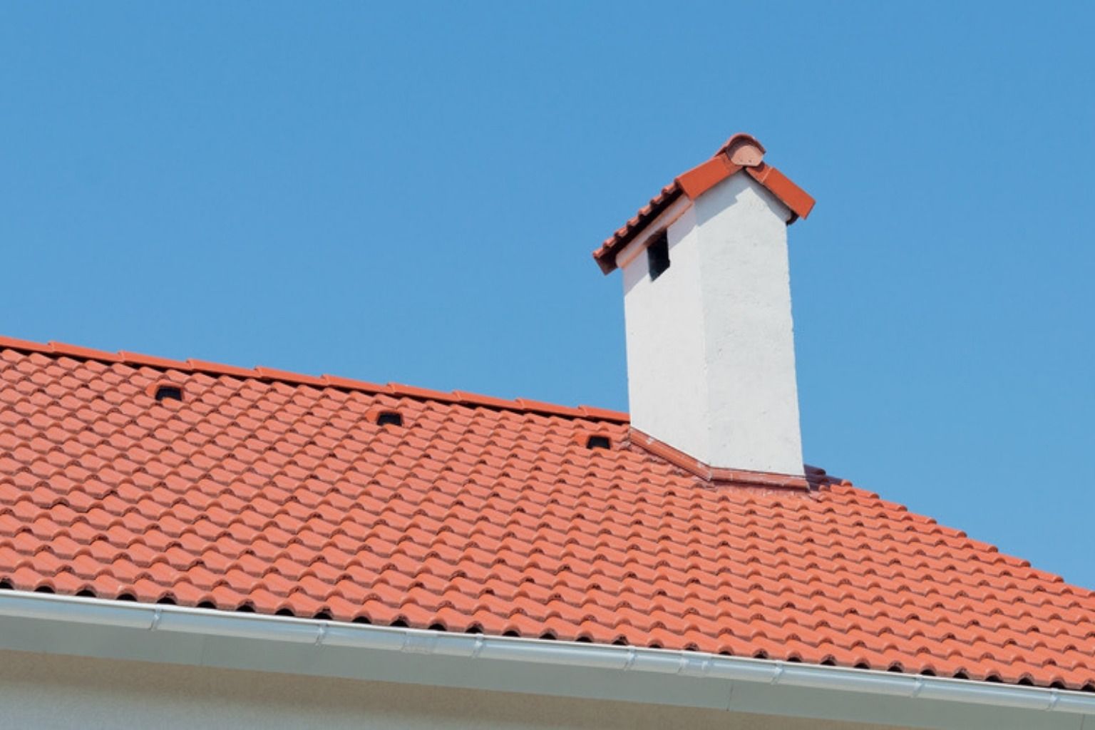 Tegltag med skorsten mod blå himmel